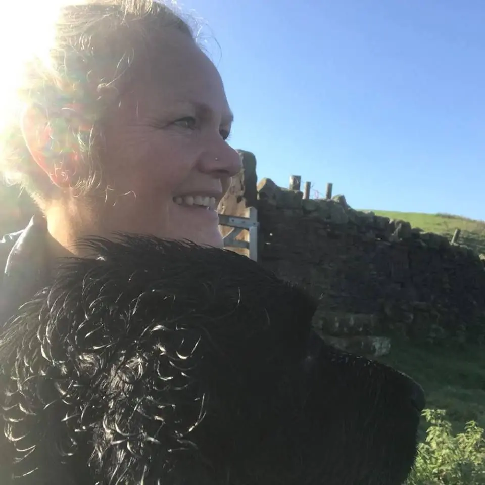 A shining photograph of a woman with short hair standing in front of a brick wall She is looking off to the side with a serious expression on her face.