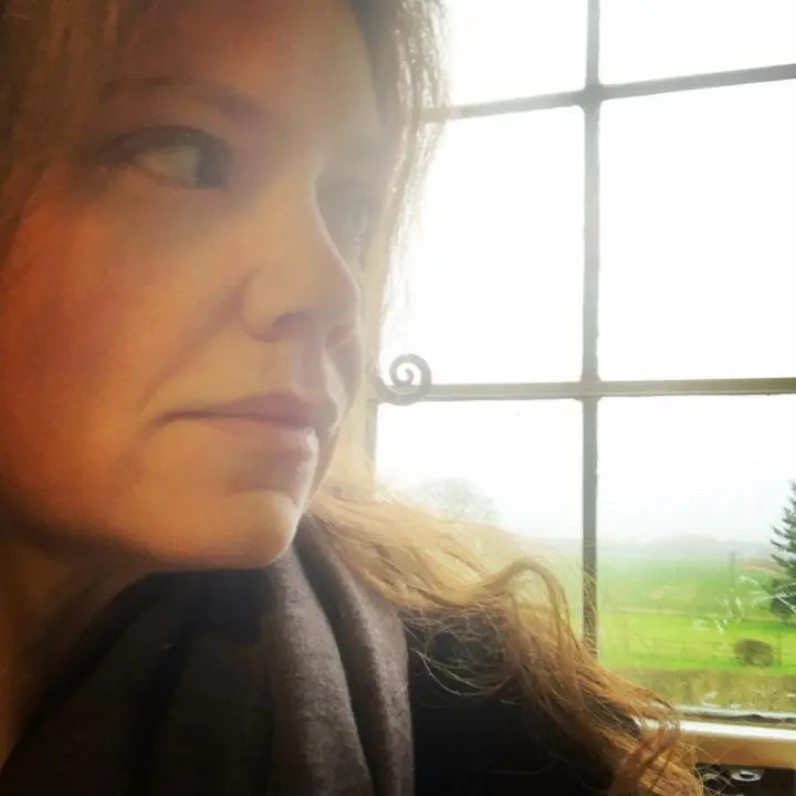 A lady standing with a window, her left side capturing the beauty of the mountain