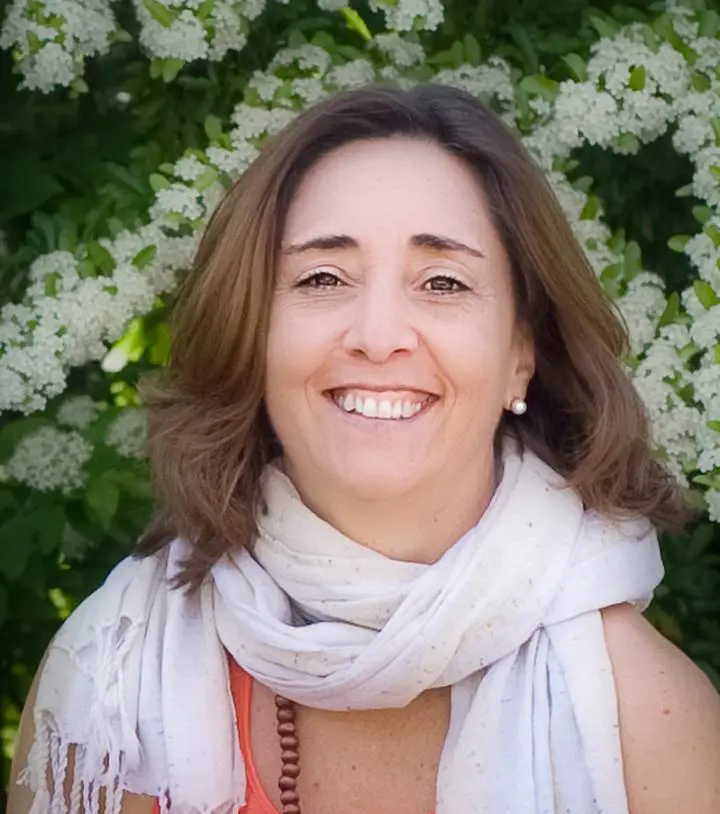 A smiley woman who has scattered hair and she is wearing piece handwoven scarf | Her background is surrounded by yoga Nidra white followers
