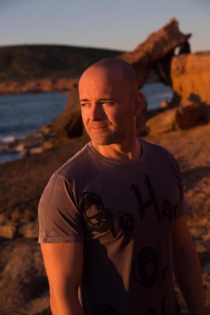 A bald Yoga instructor man standing on the beach streaming