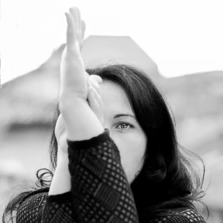 A beautiful girl is standing in a yoga pose, with flipped hands and wearing a black shirt