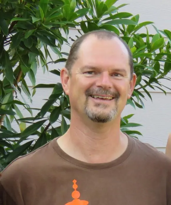 Standing under a tree Male Yoga instructor wearing a brown T-shirt