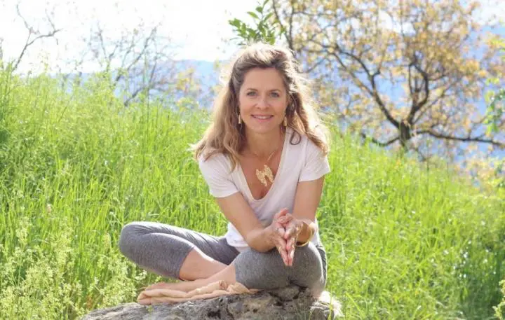 A young lady sitting on a stone with their surrounded by bushes and closing her hand as a yoni shakti style