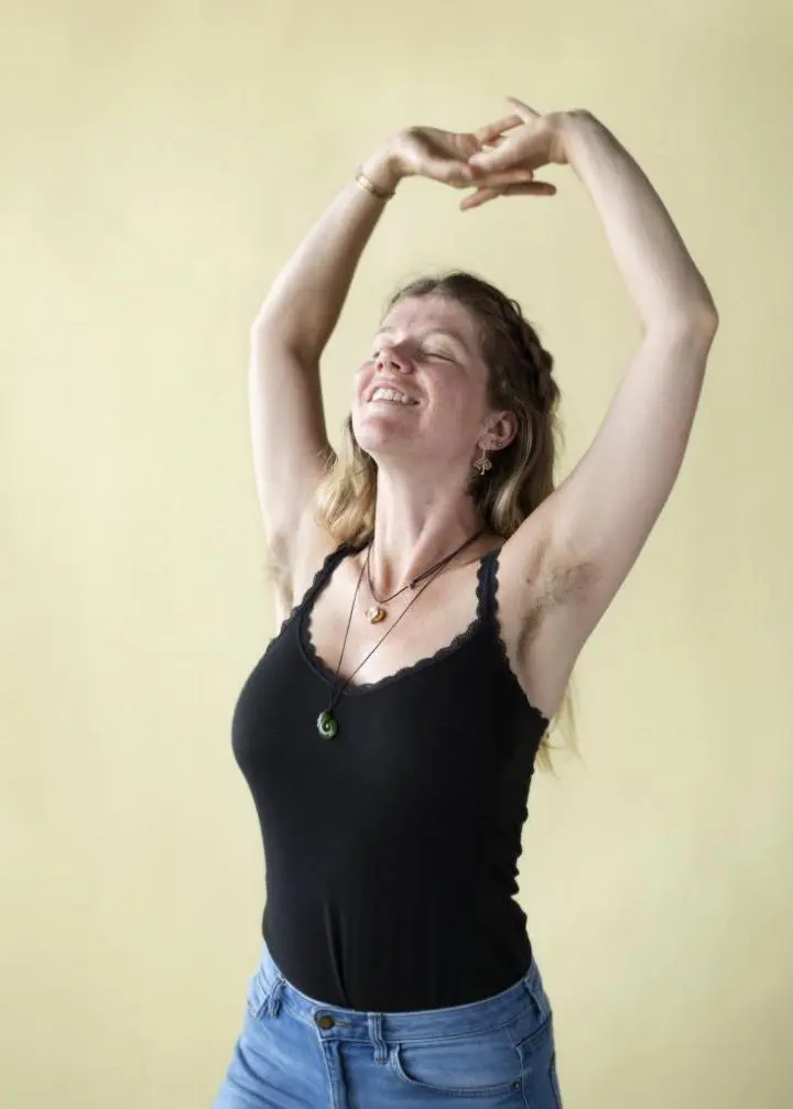 A white-skinned girl wearing a black shirt with her arms & face upward, standing in a yoga pose