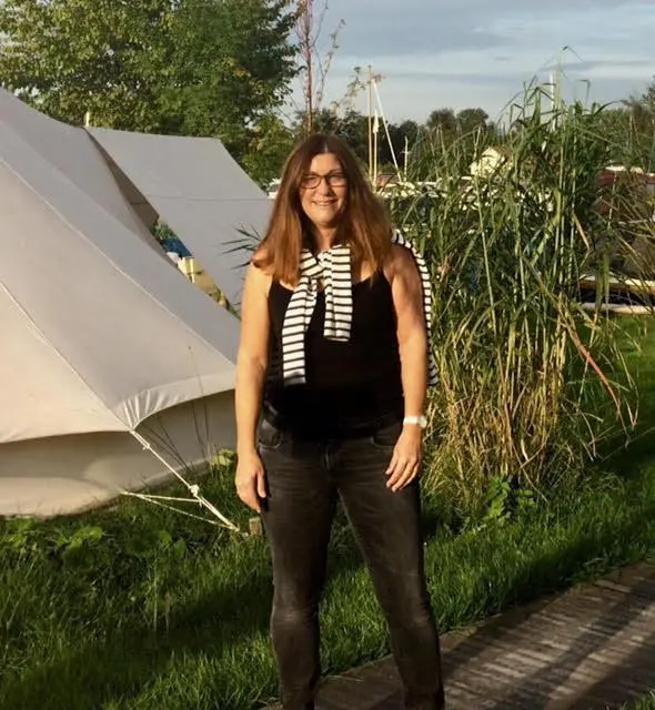 A fat woman standing on the road with her background in camp & bushes