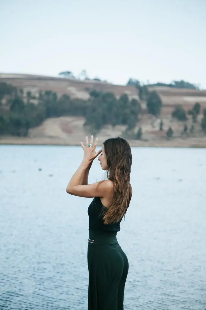 An aesthetic girl standing on the beach of the river with The Helpful Yoga Poses & wearing a bottle green belted jumpsuit