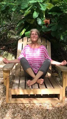 The old woman seated in Relax yoga pose on a chair on her lawn