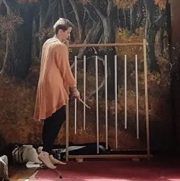 A woman standing in the massage room, with tree painted wall and some yoga instruments on the ground