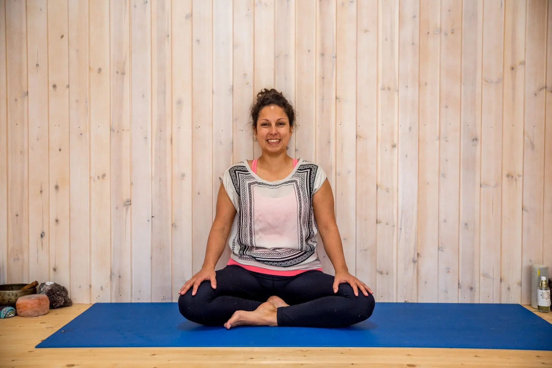 A healthy woman sitting on a blue sheet & leans against a wall, practicing Pose of Yoga week