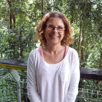 A smiley old woman standing on the roof of Relax Massage Center and her backside shows a forest