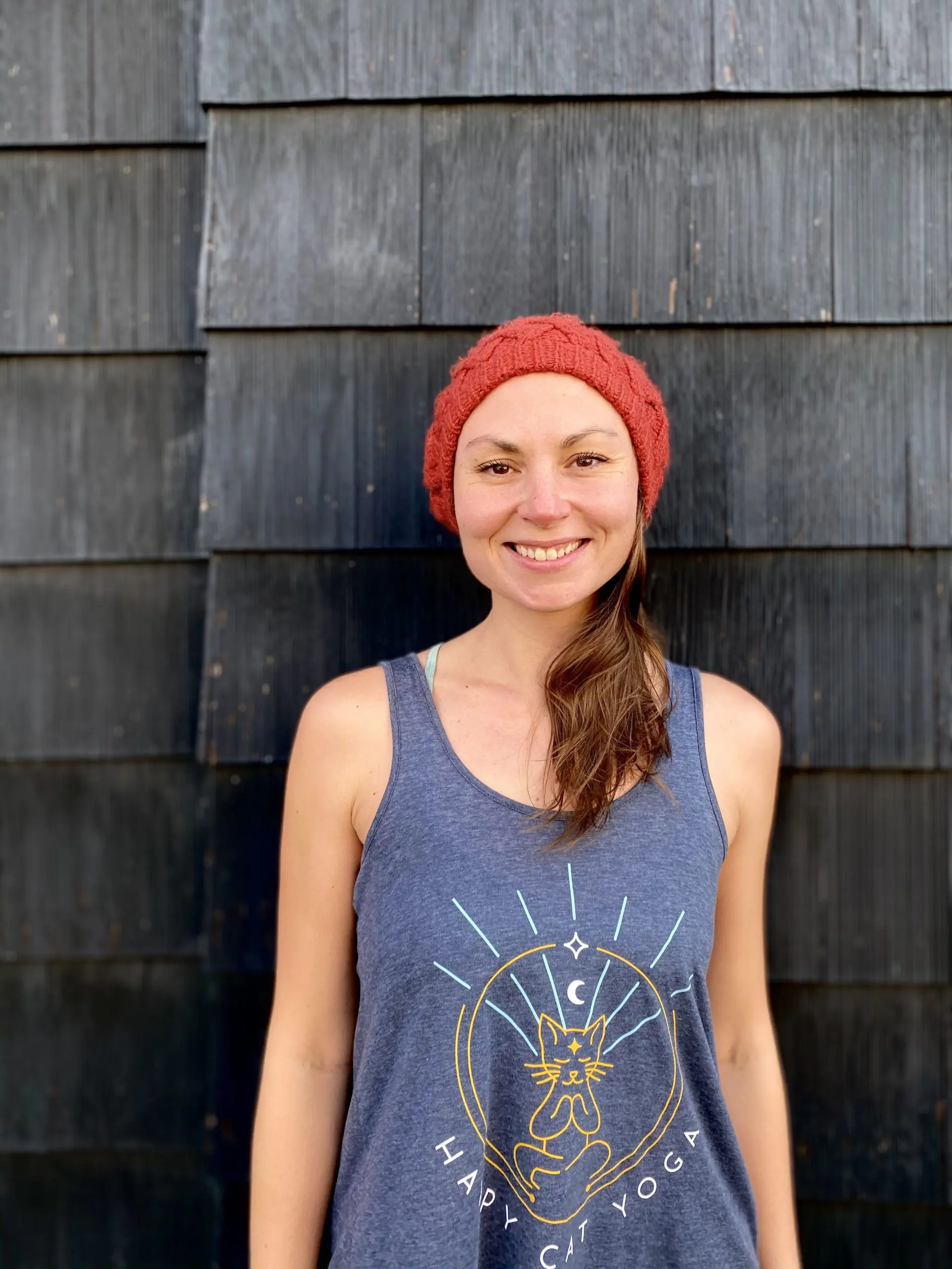 A smiley adult woman wearing a yoga black shirt in the name of "Happy Cat Yoga" written in a Calibri (Body) font