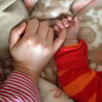 Mother's hand finger in little girl's hand on the bed