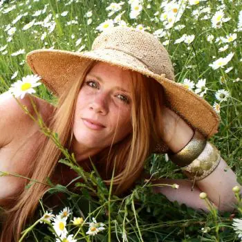 An adult girl lying in white flowers who have brown hair and wearing the cap