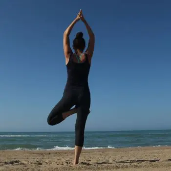 A Woman performing a backbend pose in yoga at the beach of the ocean