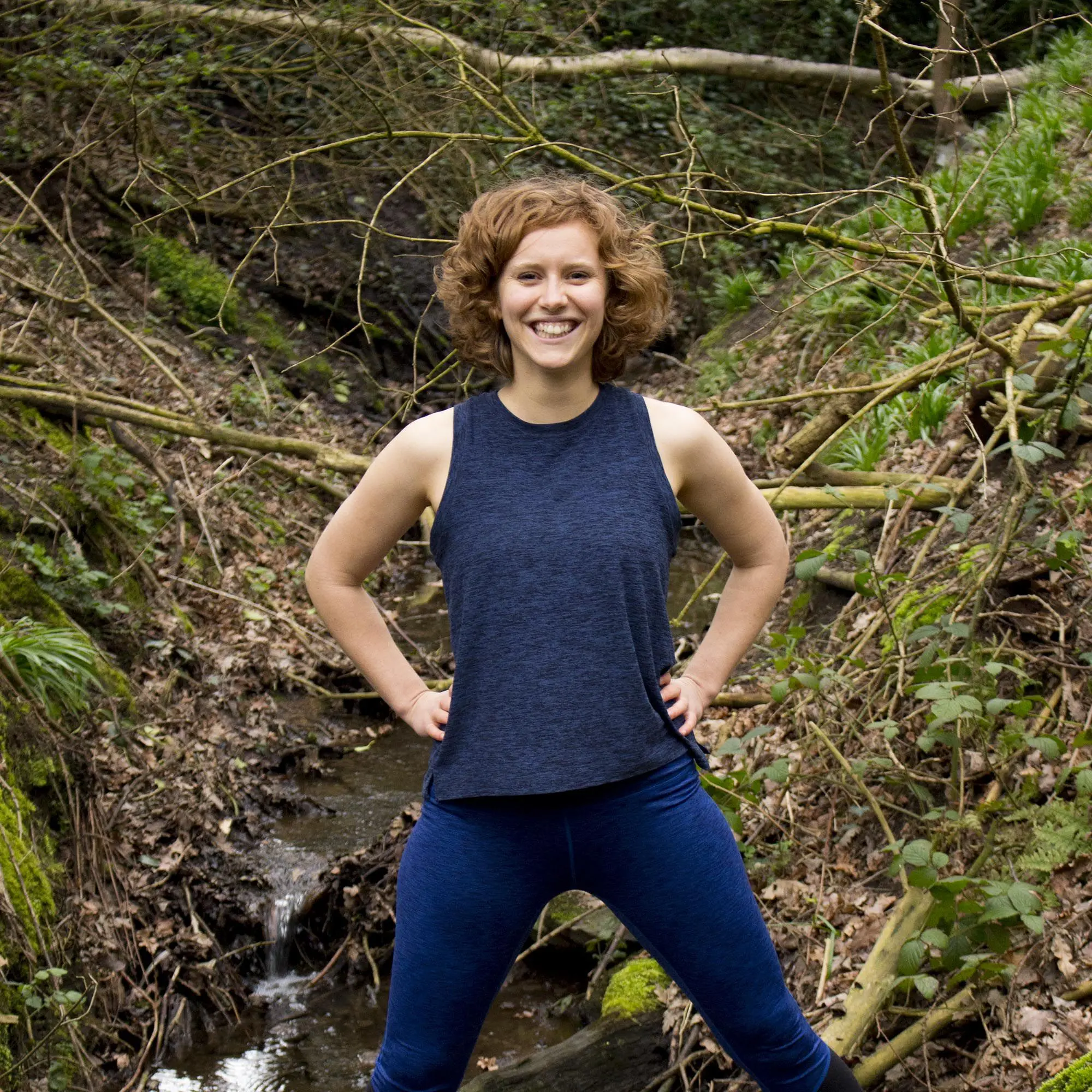 A smiling Woman performing a backbend pose in yogism, with their arms extended