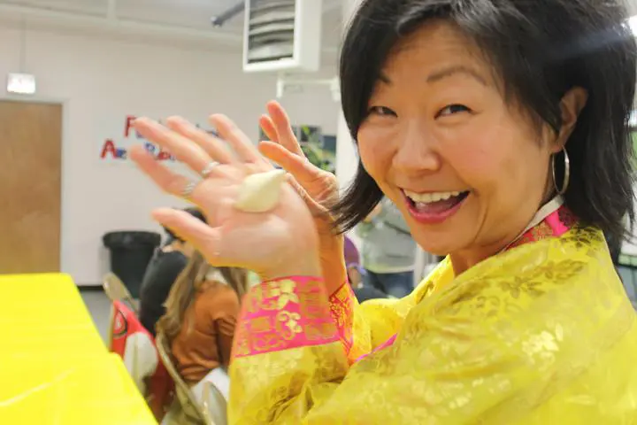 A Woman teaching a yoga class, with students following along and holding a piece of dough