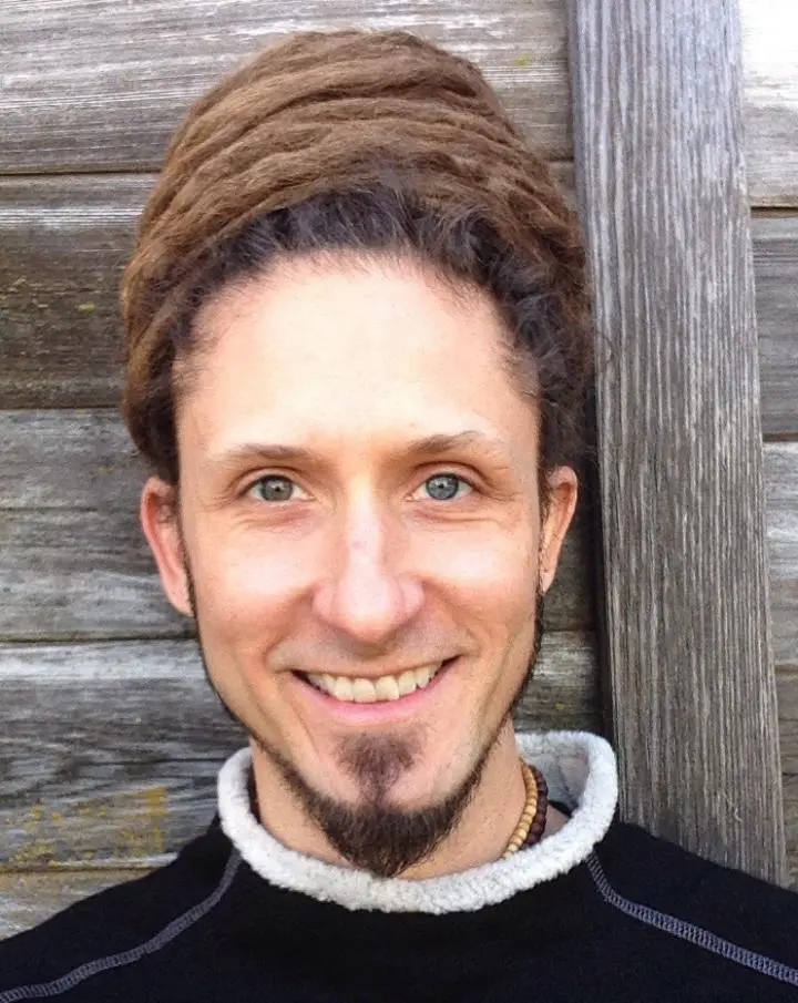 A smiley man standing to leans at the Yoga Nidra's wood-type door