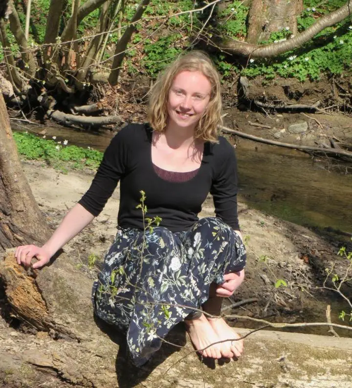 An aesthetic adult girl wearing a black shirt, sitting on a lying tree & her backside streaming stream