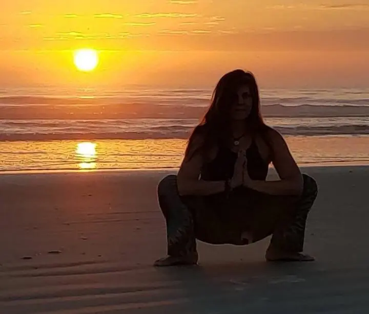Younger woman sitting at the sunset view of the beach of the ocean with the yoga pose