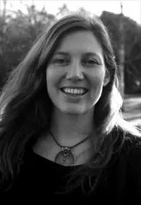 In a black, and white photo, a smiley yoga teacher who wears necklaces