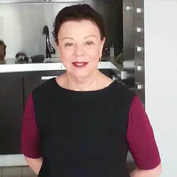 An old woman standing in Yoga Nidra's kitchen is wearing a black suitor