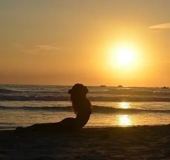 A young woman lying on the beach of see in a yoga pose with a sunset over a beautiful natural landscape