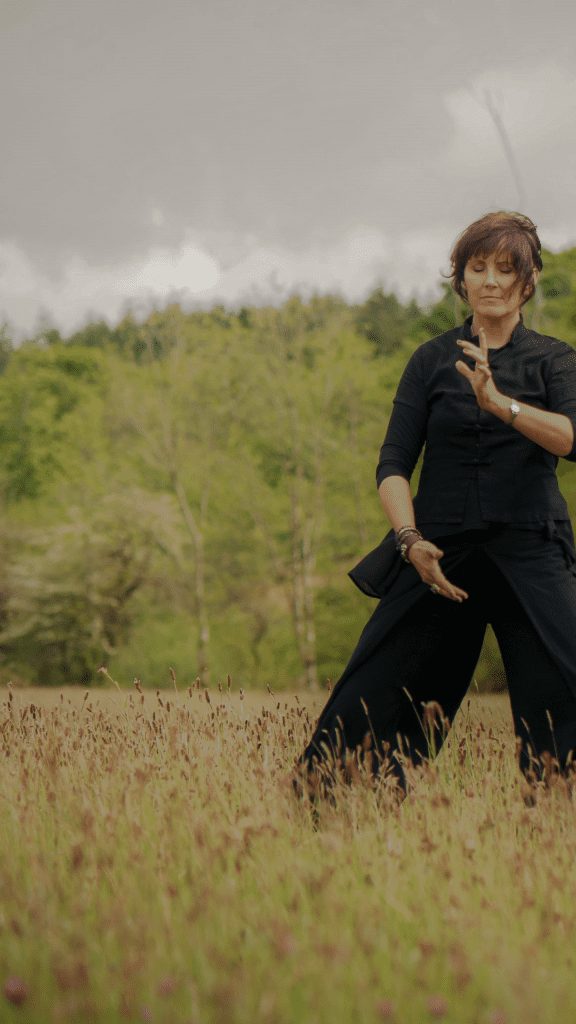 A young female standing in the field with the Womb Yoga pose, with her body twisted and her arms twist