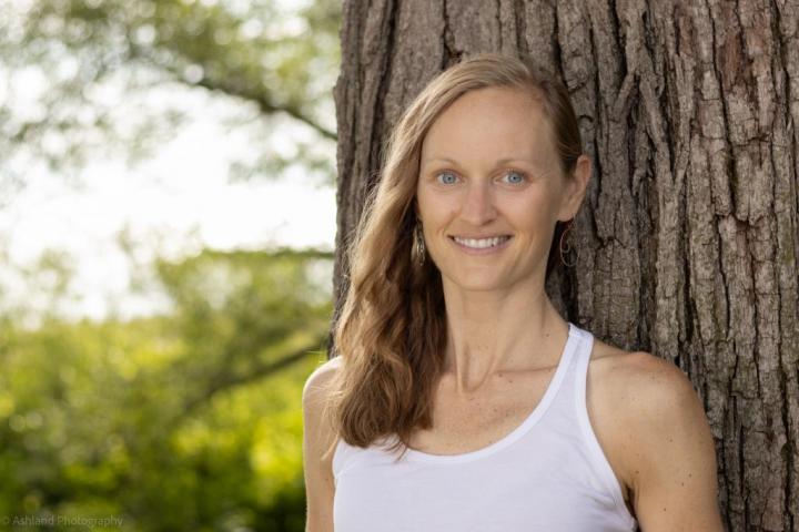 The brown eyes woman leans at the tree and she is wearing a practicing yoni shakti yoga dress