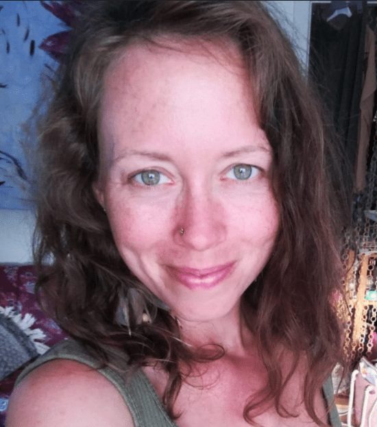 Brown eyes and scattered hairs woman standing in Nidra's massage room, surrounded by a textured background