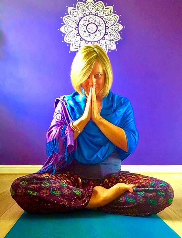 She sitting in a meditative pose with their eyes open, surrounded by a textured background