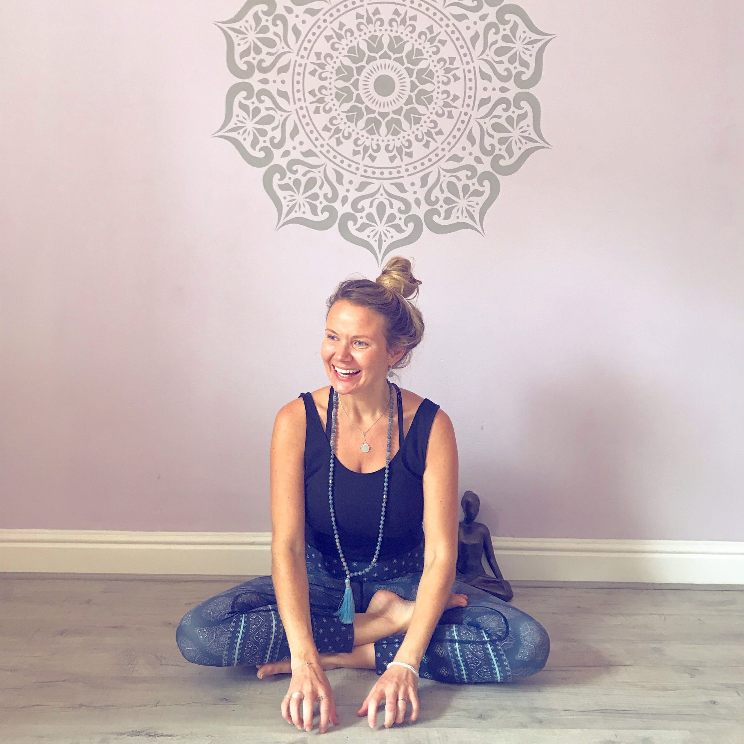 A smiley female sitting on the ground in a meditative yoga pose, with the back side, keeping a Statue