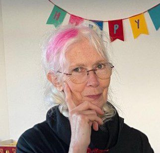 The old woman who her white hair and wearing glasses with a smiley expression, her backside written "HAPPY YOGA JOURNEY"