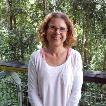 A smiley old woman standing on the roof of Relax Massage Center and her backside shows a forest