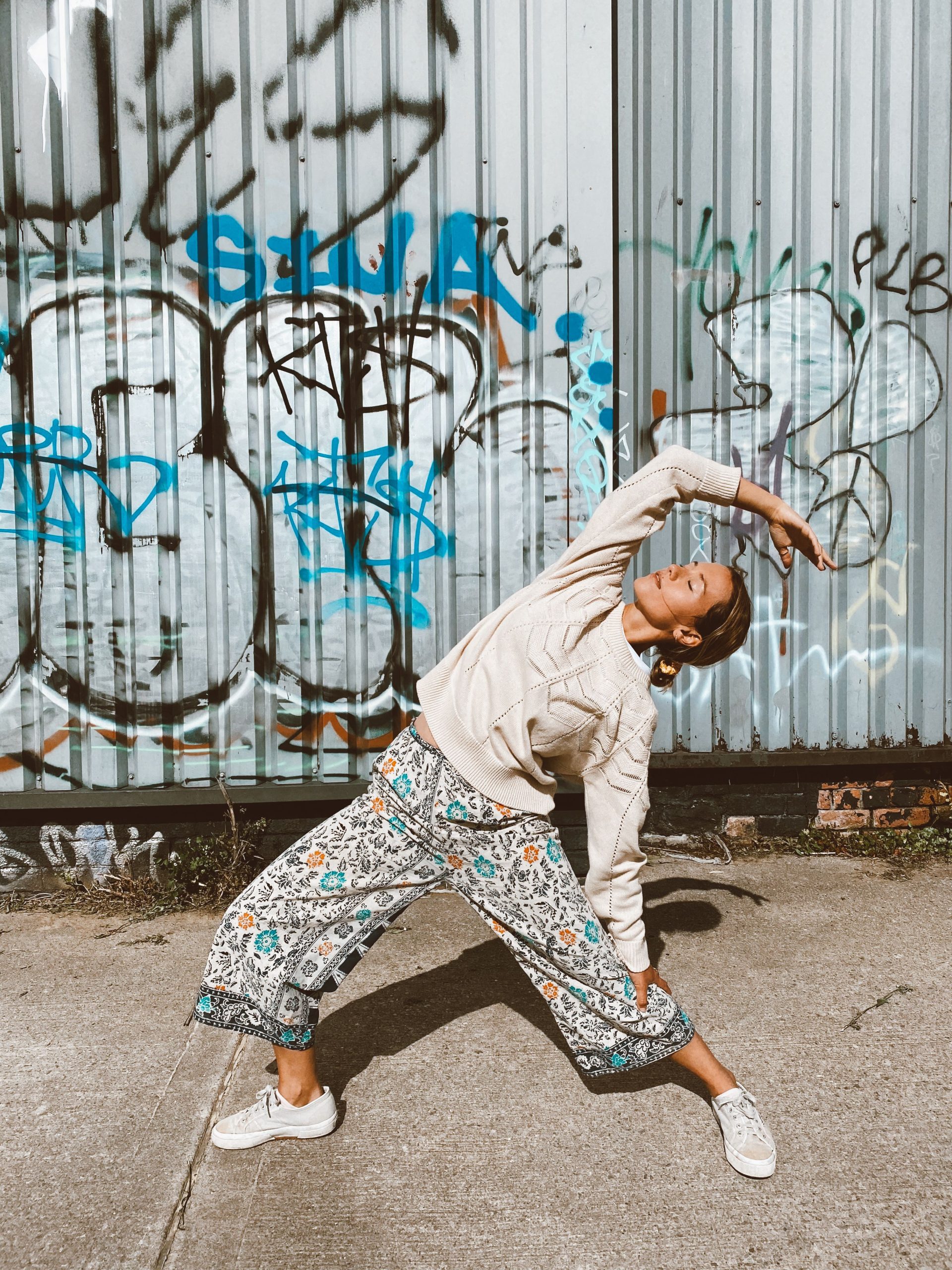An adult girl standing in YIN YANG Yoga pose in front of a colorful wall