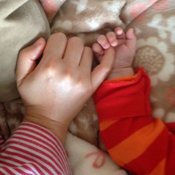 Mother's hand finger in little girl's hand on the bed