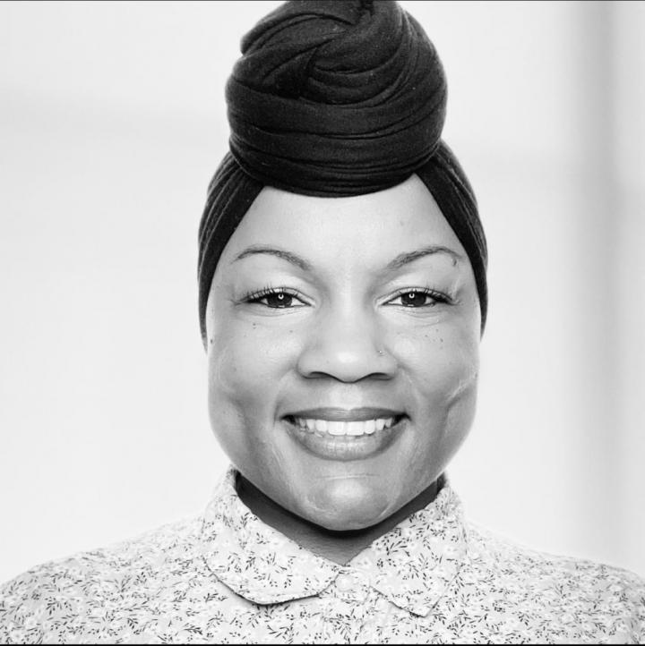 In a black, and white photo, an African Therapy Teacher woman tying a BRON headband - black