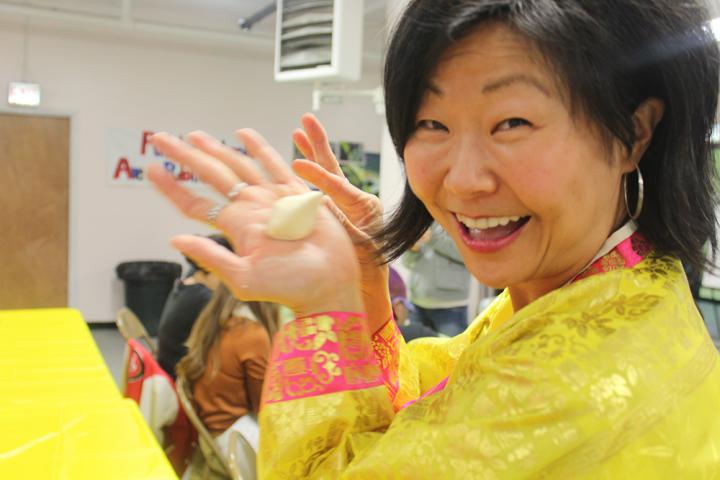 A Woman teaching a yoga class, with students following along and holding a piece of dough