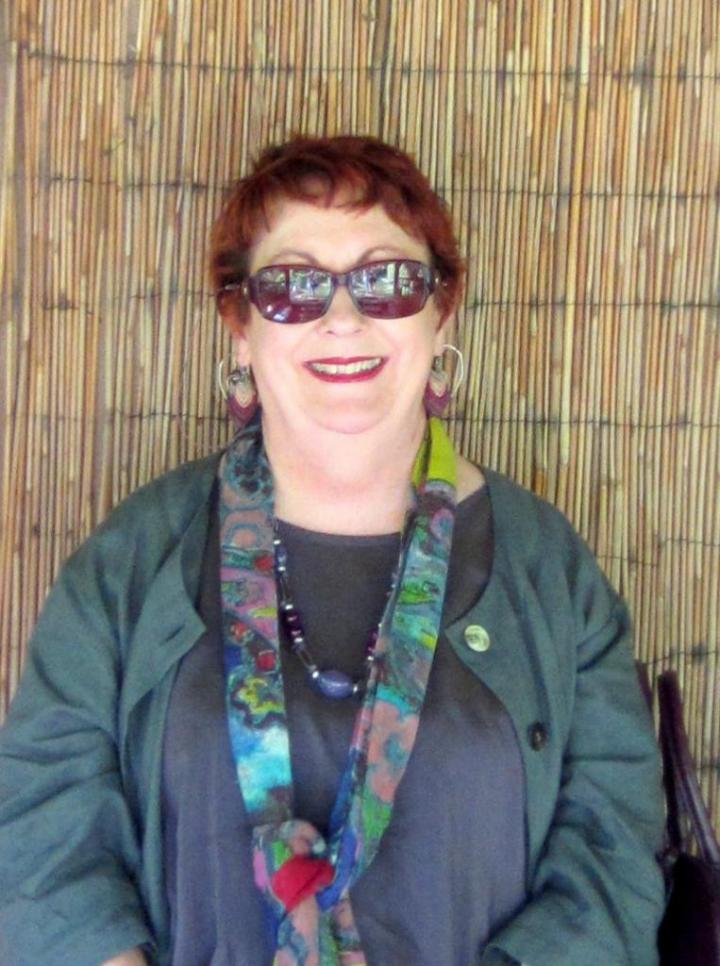 The old woman is standing in a chiropractic hut and wearing a handwoven scarf and glasses.