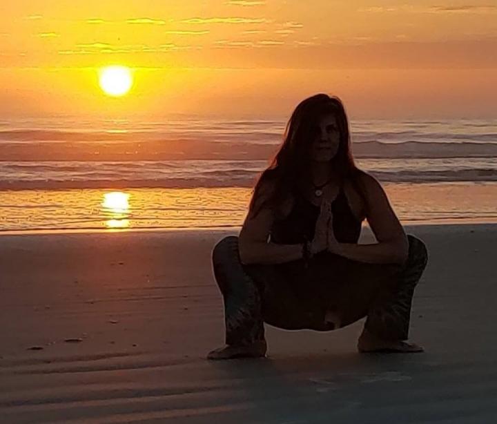 Younger woman sitting at the sunset view of the beach of the ocean with the yoga pose