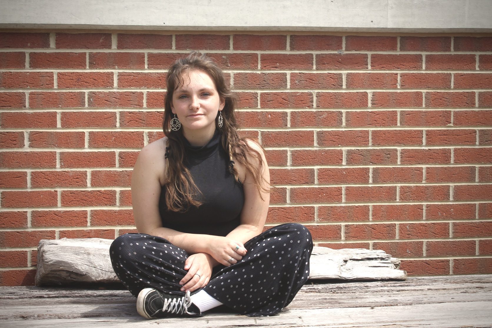 An adult lady sitting on the road and his backside school wall & wood piece