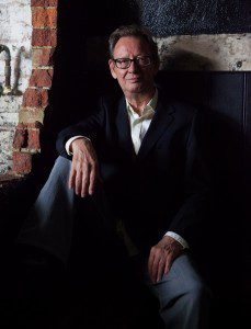 A glasses man sitting in a chiropractic room with the left-side wall hole